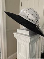 Side angle of the black wide brim sun hat with a white polka dot scarf tied around the crown.