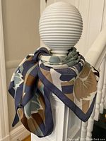 Photo showing the scarf draped around a spindle, displaying the pattern and colors including blue, beige, cream, and brown shades.