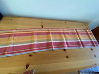 Cotton striped placemats laid out on a wooden table, showing horizontal stripes in red, orange, yellow, and white.