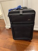 Front view of closed black Skyway suitcase with two external zippered pockets and padded handle wrapped in blue protective cover.