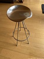 Full view of polished metal stool showing concave seat, four legs and circular footrest