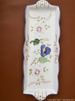 Overhead photo of a rectangular ceramic tray with hand-painted floral patterns placed on a brown surface.