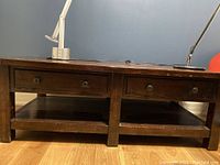 View of the front of the coffee table showing two drawers and two open lower shelves, dark wood and country style.
