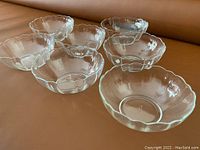 Seven clear glass bowls with scalloped rims arranged on an orange surface.