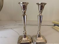 Pair of silver plated candlesticks on a marble surface.