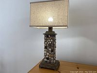 Front view of stone lamp with pebble inlaid column base and rectangular fabric shade, showing overall proportions and texture.