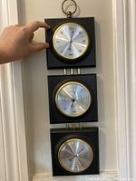 Photo of the full weather station showing three connected dials on black wood with brass rings.
