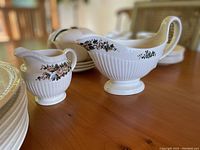 Creamer and gravy boat in foreground with stacked plates behind