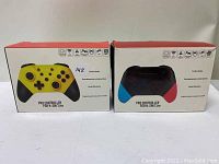 Front view of two boxed pro controllers for Nintendo Switch/Switch Lite, yellow and black design and multicolor design