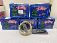 Five boxed LED string lights with the box design showing a Christmas tree and 'Multi Function' label. The photo shows one coiled LED string light and one remote control in front of the boxes.