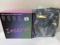 Photo of Inscrok Ultra-Long LED Strip Lights original packaging next to the coiled LED strip wrapped in silver protective plastic.
