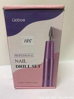Front of box showing the product name, brand and a large image of the purple handheld drill device.