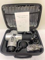 Mizzuco massage gun with attachments and accessories inside black carrying case. Manual visible inside case lid.