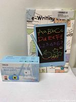 Photo of boxed Omzer kids digital camera and boxed LCD e-Writing board together.