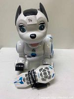 Front view of the white and blue robotic dog toy with wired remote control placed in front.