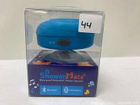 Photo of the ShowerMate waterproof Bluetooth shower speaker in original packaging, showing the blue speaker with suction base inside a clear plastic box placed on top of a blue colored display box.