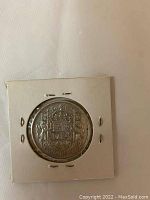 Reverse side of the 1957 Canadian 50 cent silver coin showing the crowned coat of arms of Canada mounted in a white cardboard holder.