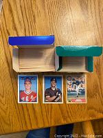 Three sample baseball cards from the collection placed next to the open boxes showing card face design and player photos.