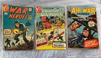 Front covers of three vintage war comic books laid out side by side on a light-colored surface. Titles are War Heroes, Fightin' Marines, and Air War Stories. Each cover features colorful war-themed illustrations with soldiers and aircraft.