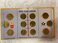 Full view of 9 gold-colored medallions affixed inside a tri-fold holder shaped and printed like a hockey rink with Canadian Olympic and McDonald's logos.