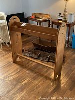 Solid wood blanket rack with curved end panels and cut-out handles, standing on wooden floor.