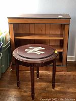 Front view of wood bookcase with black trim and round New York Yankees side table with visible large Yankees logo on top.