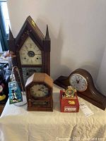 Five items on white table showing collection of clocks and lighthouse candle holder