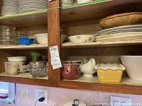 Kitchen shelf with stacked plates, clear glass bowls, yellow ceramic baking dish, and various mixing bowls