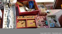 Photo of assortment of costume jewelry and personal effects on table, including red vintage lipstick tins, earrings, and small pins.