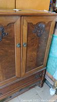 Close-up photo of the dresser's left side doors showing ornate metal decorative handles and the wood grain finish.