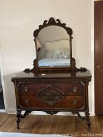 Front view of antique wooden dresser with attached arched mirror, showing detailed carvings and hardware.