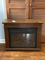 Front view of wood-finished electric fireplace with faux logs visible behind glass panel