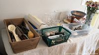Overview of flatware and kitchen utensils in wooden and plastic containers atop a white cloth.