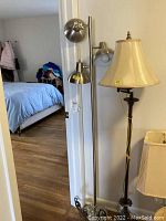 Photo of metal floor lamp showing three adjustable round metal lights and vertical pole against wall.