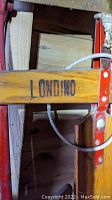 Close-up of red metal steering bar with wooden crossbar labeled 'LONDINO'