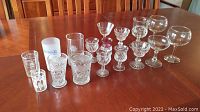 Collection of various types of glassware including stemware, cordial glasses, and drinking glasses arranged on wood table