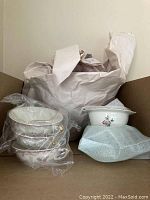 Wrapped china pieces packed in box including bowls and cups with floral pattern