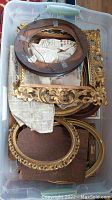 Container with multiple vintage and gilded picture frames, showing a variety of shapes including oval and rectangular with wear and damage.
