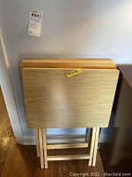 Two rectangular wood folding TV trays stacked against wall