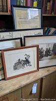 Photo showing multiple framed artworks arranged against a bookshelf, including the silhouette image and the vintage certificate in black frame.