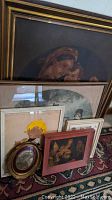 Photo showing multiple framed artworks including large pastel Virgin Mary portrait and smaller framed pieces leaning together.