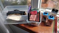 Overall lot showing plastic bins with wallets and gloves, plus watch band boxes arranged on window ledge
