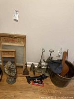 Photo showing two antique washboards; wooden framed with metal surfaces, a figurine candle holder of a robed religious figure, metal irons, iron Dachshund-shaped scraper, nutcracker, cauldron, and fire flower decorations.