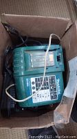 Photo showing one Makita DC18RA battery charger inside a cardboard box with cords.