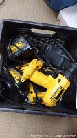 Photo showing two DeWalt cordless drills and two chargers in a black plastic crate. Drills are yellow and black with XR labels visible.