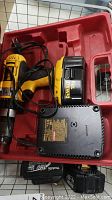 Photo of a yellow and black DeWalt cordless drill with 18V battery, charger and Makita 18V battery inside a red plastic case