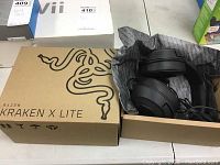 Photo of the Razer Kraken X Lite headphones partially out of the box wrapped in paper, showing the headphones and the box with the Razer logo.