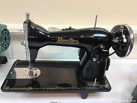 Side view of the Hamilton black sewing machine with gold decoration and brand name.