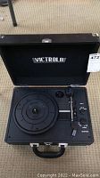Victrola turntable open in suitcase-style case, showing the turntable platter, tonearm, and carrying handle.