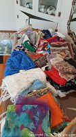 Photo of assorted vintage scarves piled on a table showing various colors, textures, and patterns, with visible fringed edges and mixed fabrics.